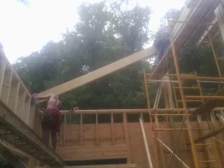 Carpenter raising a rafter beam on a new second story frame in Dixon